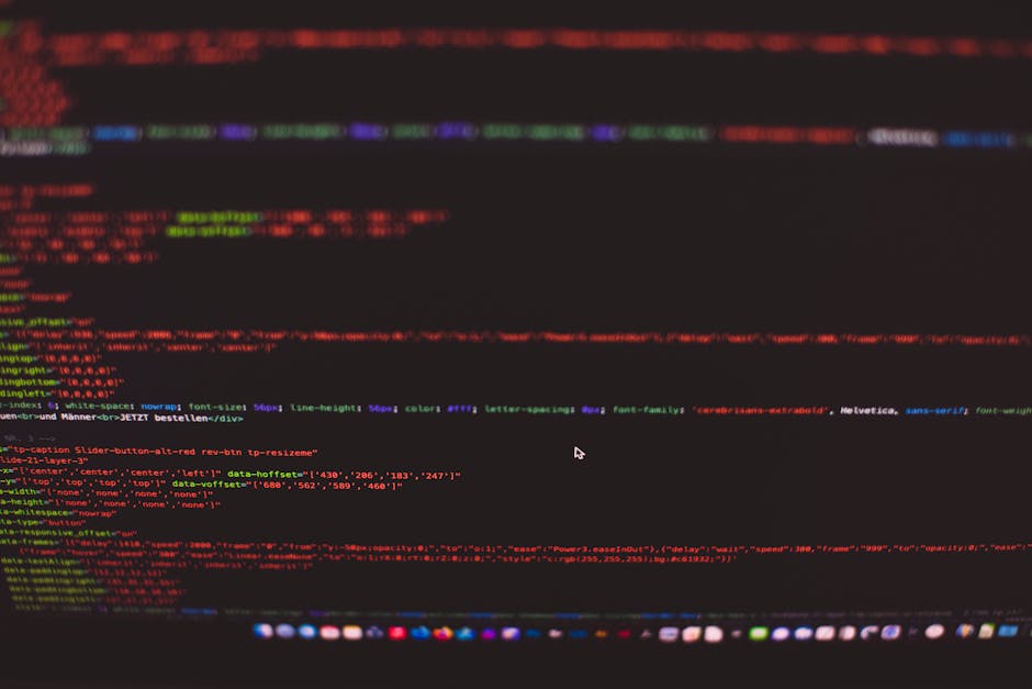 A close-up view of a person's hand typing on a laptop keyboard placed on a wooden surface. The screen displays lines of code or web development text with colorful syntax highlighting, indicating activ